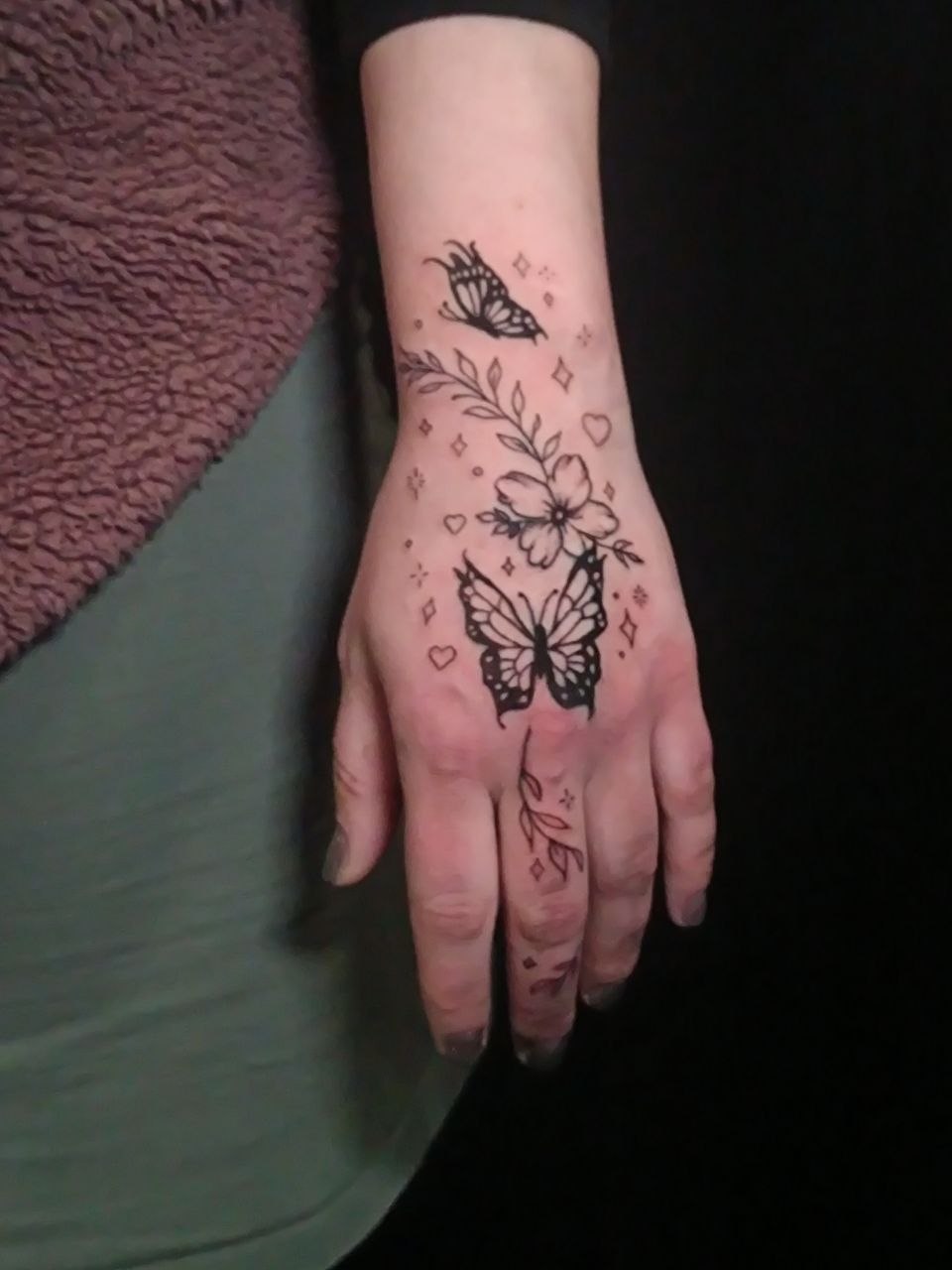 Tattoo eines Schmetterlings mi Blumen und Ornamenten auf dem Handrücken und Handgelenk
